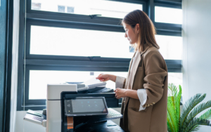 Smiling Young Business Woman Holding Document While At Printer