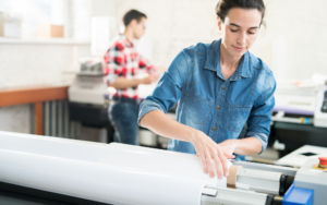 Young Woman With Hair Bun Loading Wide Format Printer