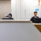 Healthcare Staff Speaking Into Headset At Clinic Desk With Monitors