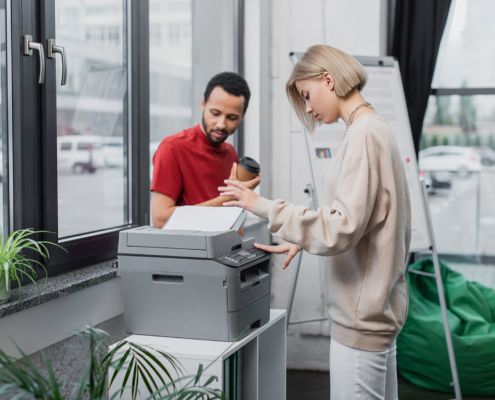 Blonde Woman Copying Document Near African American Manager With Paper Cup